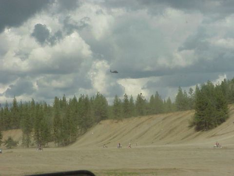 1989 Ford Bronco - Dirt bikes are ridden on a sandy hill with trees in the background and a helicopter in the sky.