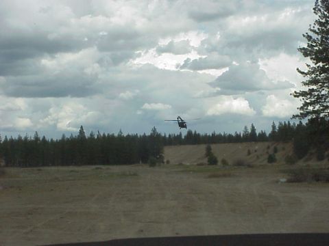 1989 Ford Bronco - A helicopter is seen in flight over a rural landscape with a dense line of trees and a cloudy sky.