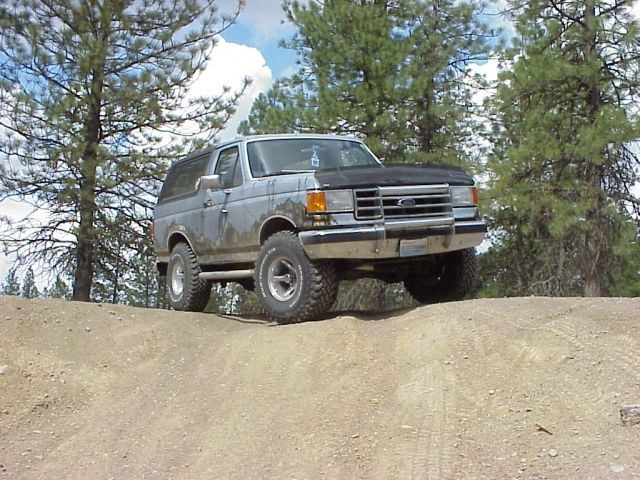 Silver Ford Bronco driving on a dirt hill with trees in the background