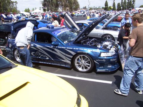 2002 Ford Mustang - A customized blue coupe is displayed at an outdoor car show with its hood and doors open.