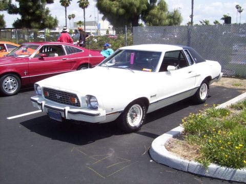 1978 Ford Mustang II - A white 1975 Ford Mustang II coupe with a black vinyl roof is parked next to a red car.