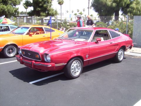 1978 Ford Mustang II - A red 1978 Ford Mustang II coupe is parked next to an orange car at a car show.