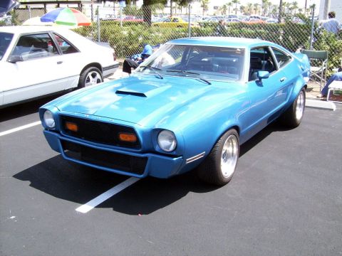 1978 Ford Mustang II - A blue coupe with a hood scoop is parked in a lot next to a white car.
