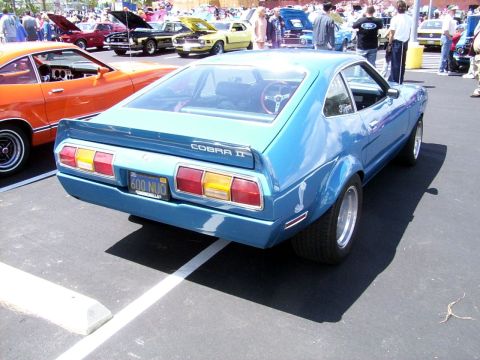 1978 Ford Mustang II - A blue 1978 Ford Mustang II Cobra II is parked at a car show, with other vehicles and people in the background.