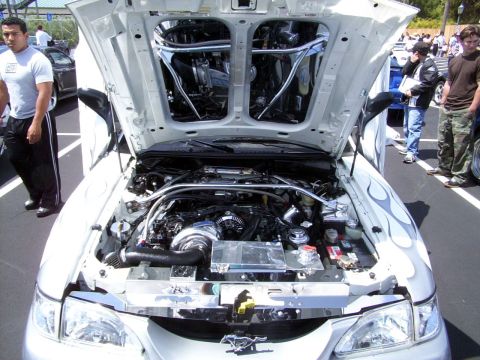 2002 Ford Mustang - A customized 2002 Ford Mustang is displayed with its hood open, revealing a modified engine and unique flame decals on the fender.