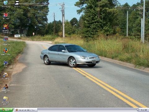 1998 Ford Taurus - Silver 1998 Ford Taurus driving on a two-lane road with yellow double lines.