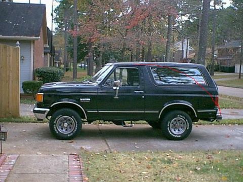 1988 Ford Bronco - A black Ford Bronco is parked on a suburban driveway with trees in the background.