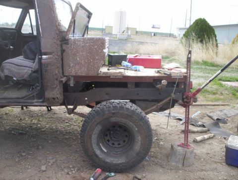 1978 Ford Bronco - This heavily soiled truck bed, equipped with a Hi-Lift jack and a red toolbox, is undergoing some work.