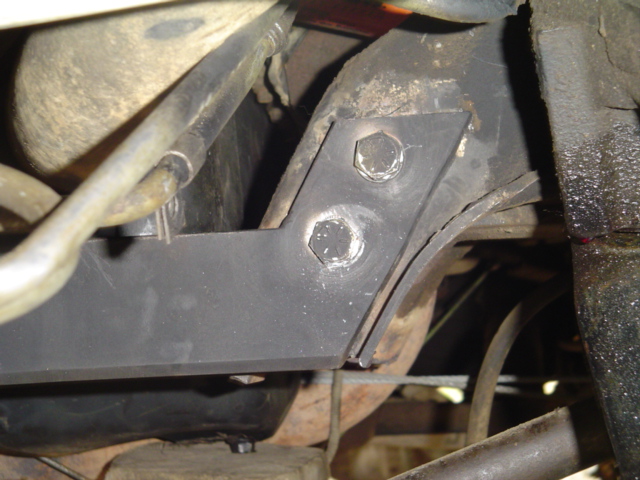 Black metal bracket bolted to vehicle frame, with metal tubes nearby