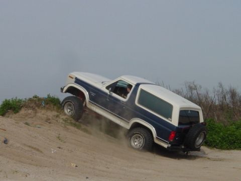 1986 Ford Bronco - This Ford Bronco is navigating a steep, sandy incline with dust kicking up from its tires.