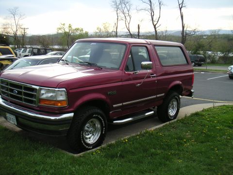 1994 Ford Bronco - A maroon Ford Bronco is parked outside on a cloudy day with other vehicles visible in the background.