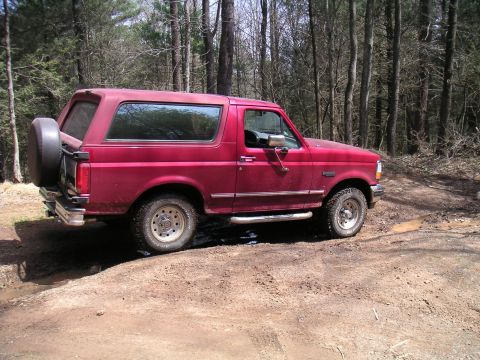 1994 Ford Bronco - A red Ford Bronco is seen from the side on a dirt path in a wooded area.