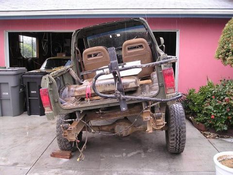 1986 Ford Bronco II - The rear of a 1986 Ford Bronco II, stripped down and damaged, sits in front of a pink garage.
