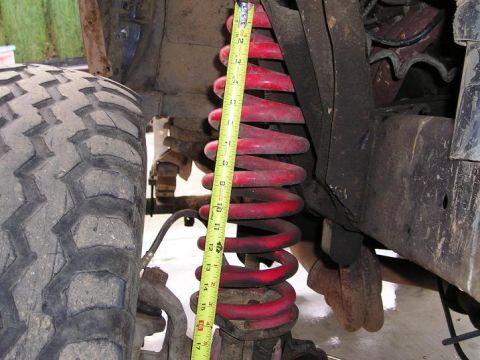 1986 Ford Bronco II - Close-up of a vehicle's suspension system, showing a tire and a red coil spring with a measuring tape.