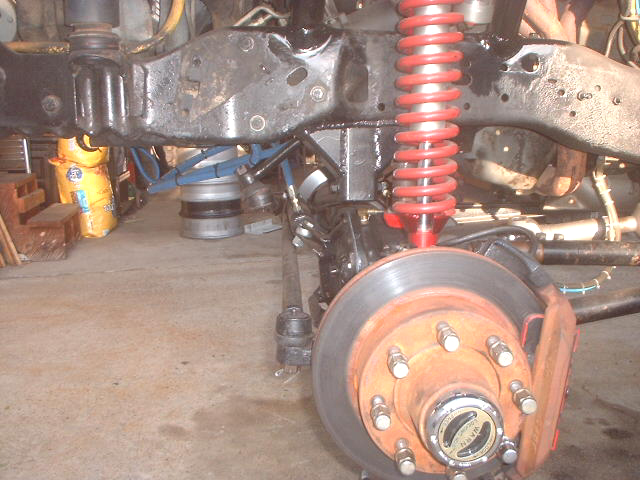 Front suspension with red coil spring, rusty brake rotor and locking hub on a lifted truck