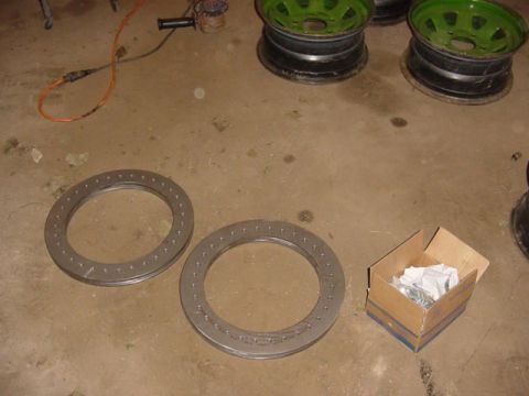 1992 Ford Bronco - Two beadlock rings and a box of fasteners are laid out on a garage floor.