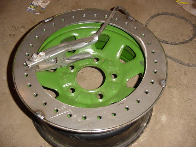 Green wheel with a metal ring bolted around its edge, showing welding marks and a clamp