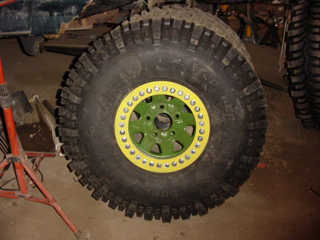Off-road tire mounted on a green wheel with yellow beadlock ring, bolted on