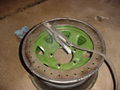 1992 Ford Bronco - A green wheel is shown with a homemade beadlock ring being welded on, with a welding clamp attached.