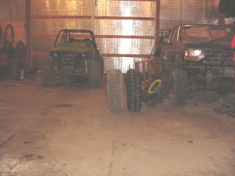 1992 Ford Bronco - Two modified off-road vehicles are parked in a garage with several spare tires nearby.