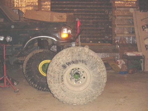 1992 Ford Bronco - A black 1992 Ford Bronco is shown with large, muddy off-road tires in a garage setting.