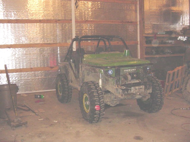 Green Suzuki Samurai with off-road tires and roll cage in garage