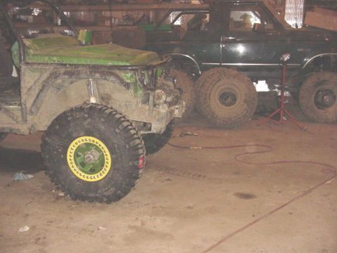 1992 Ford Bronco - Two custom off-road vehicles are parked inside a garage, one in the foreground and another in the background.