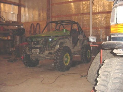 1992 Ford Bronco - An off-road vehicle with a custom roll cage and large tires sits in a garage next to another vehicle.