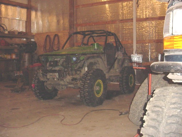Green off-road vehicle with roll cage and large tires in a garage