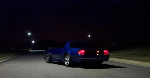 1998 Ford Crown Victoria - A blue coupe drives down a dark road at night, its taillights illuminated.