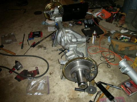 1995 Ford Bronco - A disassembled vehicle rear axle assembly sits on the floor amidst various tools and automotive parts.
