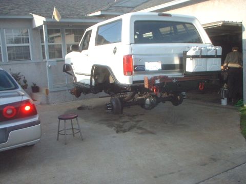 1990 Ford Bronco - A white 1990 Ford Bronco is undergoing maintenance, with its rear axle detached and suspended.