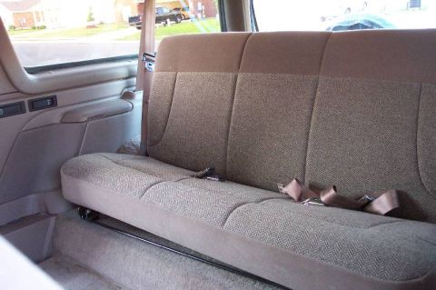 1992 Ford Bronco - Rear bench seat inside an SUV, upholstered in tan herringbone cloth with matching tan lap belts, door panel and carpet. Suburban houses and…