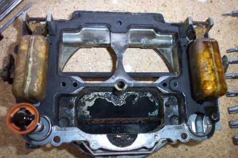 1968 Ford F-100 - The underside (air horn) casting of a disassembled carburetor showing two float bowl chambers, twin fuel float assemblies with amber/rust d…
