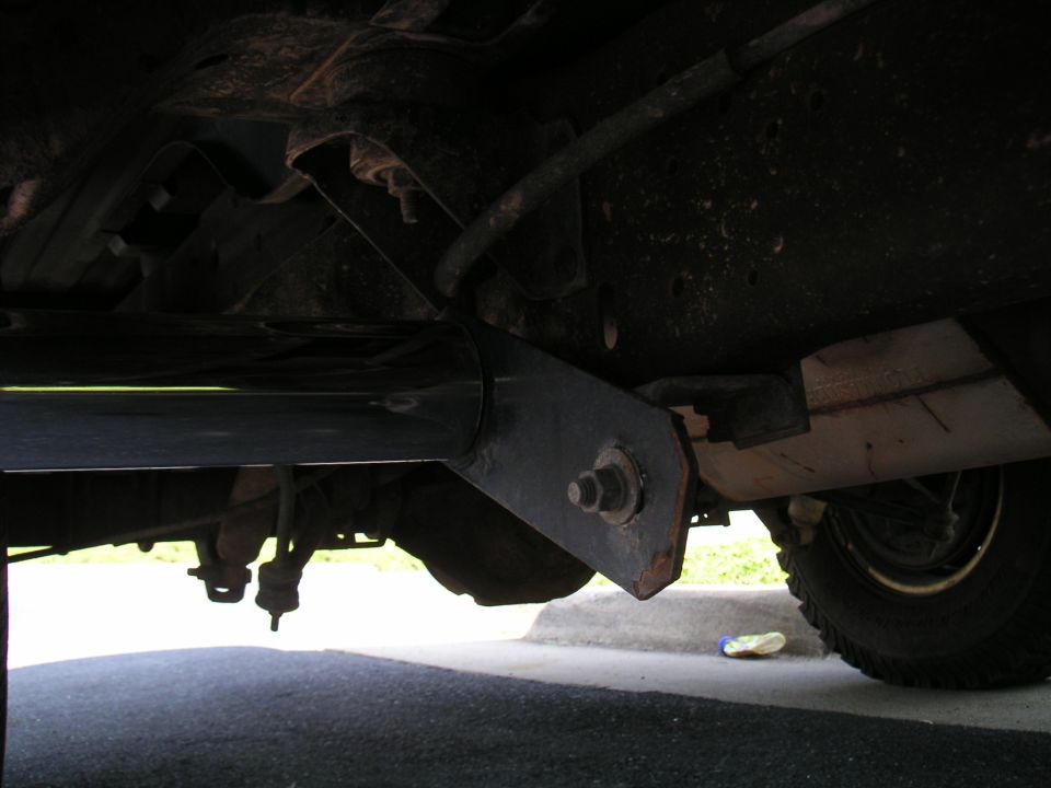 Underside of vehicle showing frame, suspension, and step bars. Tire visible on right