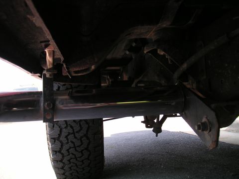 1994 Ford Bronco - Low-angle view under a truck showing a polished stainless muffler and exhaust pipe running along the frame rail, supported by a welded hang…