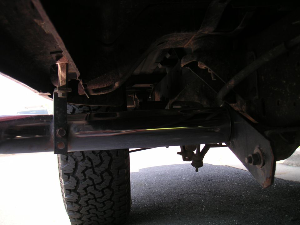 Polished stainless muffler and pipe routed along the frame rail under a truck