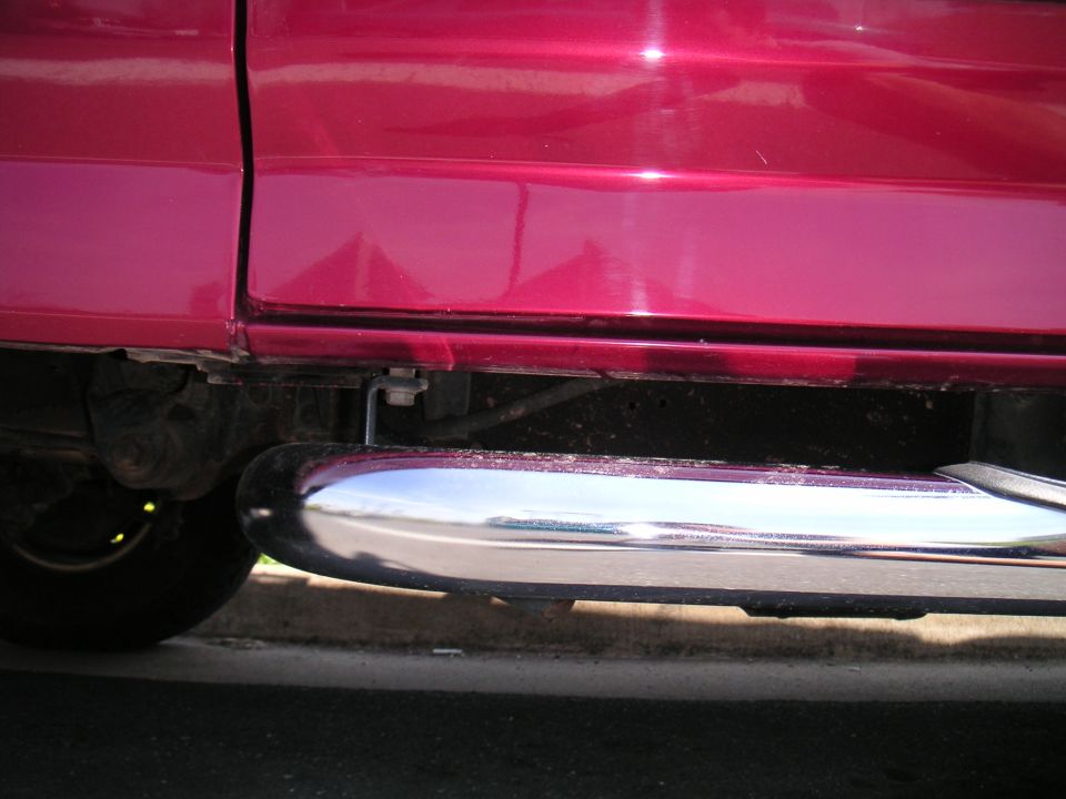 Chrome tube side step mounted under the red rocker panel of a truck
