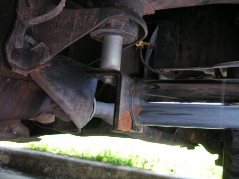 1994 Ford Bronco - Underbody close-up of a polished stainless exhaust muffler and tailpipe hung from a rusty bracket and rubber isolator beneath a truck frame…