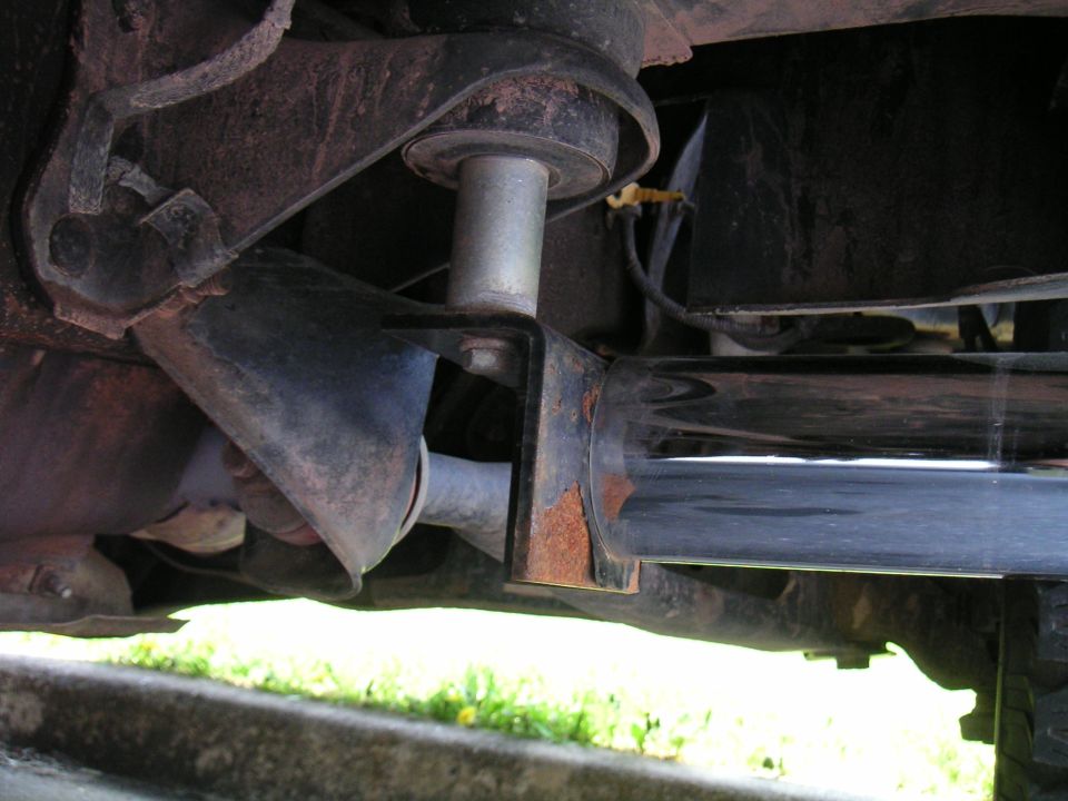 Polished exhaust muffler hung from a rusty bracket under a truck frame