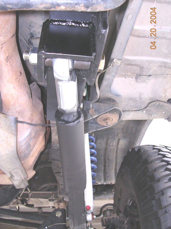 Underside suspension bracket with black shock, aluminum link and blue coil spring on a lifted 4x4.