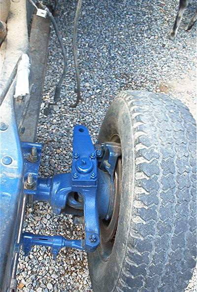1986 Ford Bronco - Close-up of a vehicle's steering linkage and tire, set against a gravel background.