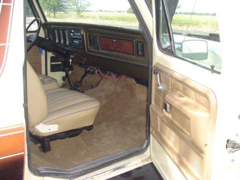 1979 Ford Bronco - The interior of a 1979 Ford Bronco features tan upholstery, a wood-grain accent on the dashboard, and a plush carpeted floor.
