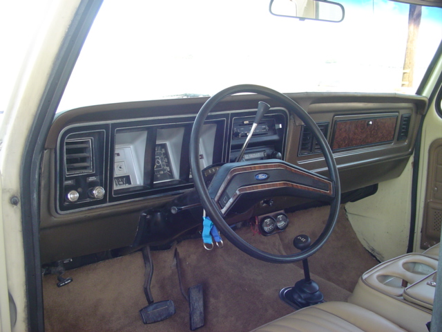 1979 Ford Bronco interior dashboard with wood grain trim, a Ford steering wheel, and brown carpet