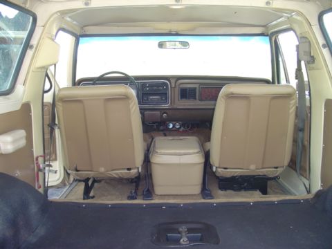 1979 Ford Bronco - The interior of a beige SUV is shown, front bucket seats, a dashboard with radio, and a portable cooler between the seats.