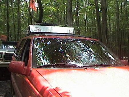 1979 Ford Bronco II - A red SUV with a roof rack and a cracked windshield is parked in a wooded area next to another vehicle.