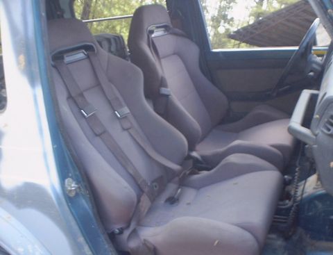 1989 Ford Bronco - The interior of a vehicle features two bucket seats equipped with racing harnesses and a steering wheel.