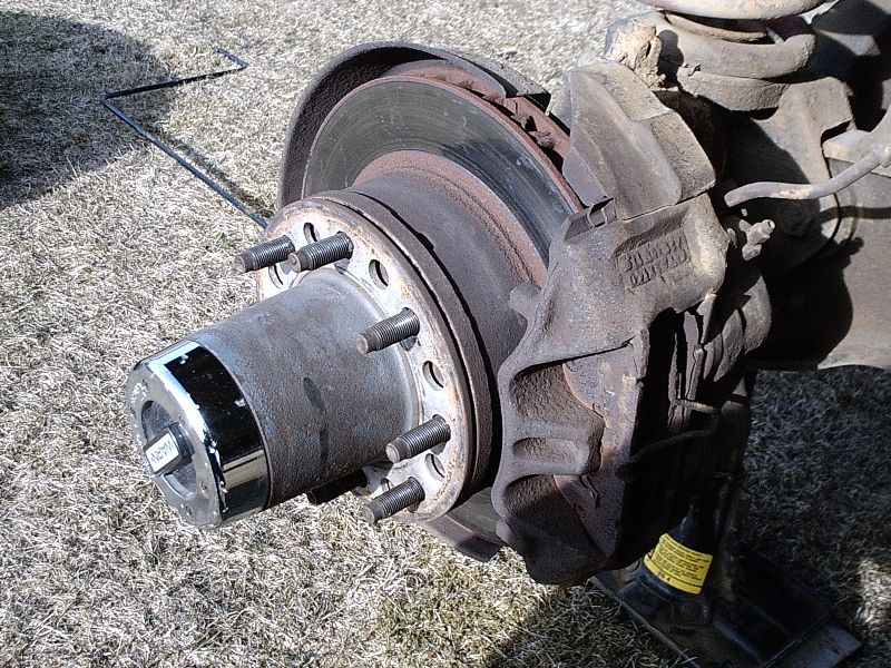 Rusty front brake rotor and hub with exposed lug studs and chrome dust cap on grass