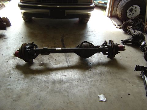 1993 Ford Bronco - A vehicle's rear axle assembly is shown on a concrete floor, with parts of a vehicle and tires visible in the background.