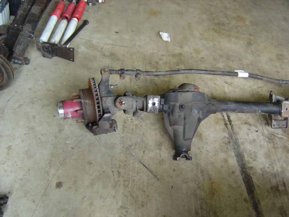 Removed solid front drive axle with differential housing, brake rotor and hub on a shop floor